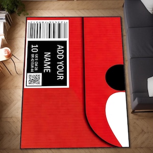 Puede incluir: Una alfombra roja grande con un diseño blanco y negro, que se asemeja a una caja de zapatos. La alfombra presenta una etiqueta negra con el texto "ADD YOUR NAME" y una etiqueta de talla con "10" y medidas en tallas UK, CM y EUR.