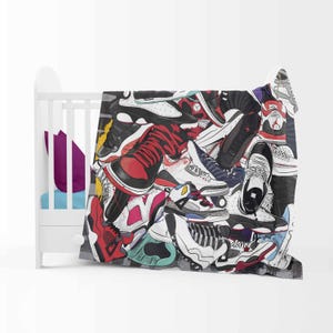 May include: A blanket featuring a colorful collage of sneakers in various styles and colors, including red, black, white, and blue. The blanket is draped over a white crib.