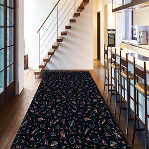 May include: A black rectangular rug with a repeating pattern of pink, blue, and yellow geometric shapes. The shapes include triangles, circles, lightning bolts, and other abstract designs. The rug is placed on a wooden floor in a hallway.