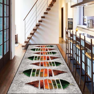 Puede incluir: Una alfombra rectangular gris con un diseño de hojas. Las hojas son en tonos de verde, naranja y marrón, con un fondo texturizado. La alfombra está colocada en un pasillo con una escalera.