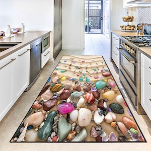 Puede incluir: Una alfombra de cocina rectangular con una escena de playa con piedras de colores, conchas marinas y arena. El diseño de la alfombra incluye una variedad de colores, incluyendo rosa, verde, blanco y naranja, creando un aspecto vibrante y naturalista.