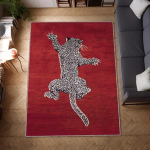 May include: A rectangular red area rug featuring a large leopard design in black and white. The leopard is depicted in a leaping pose, with its body covered in spots. The rug has a thin, light-colored border.