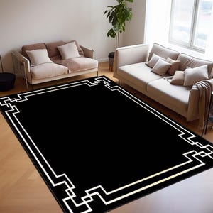May include: A large black area rug with a white geometric border. The rug is rectangular and placed on a hardwood floor. The room features two sofas and a plant, creating a modern living space.