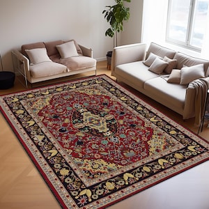 May include: A large, rectangular area rug with an ornate, traditional design. The rug features a deep red central field with a detailed floral and geometric pattern in shades of gold, blue, and green. A dark border frames the design.