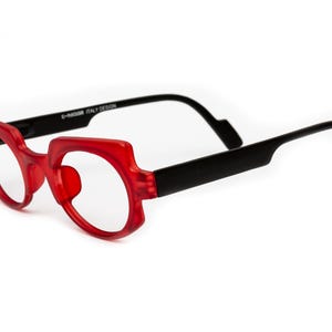 Könnte beinhalten: Rote Kunststoffbrille mit schwarzen Bügeln. Die Bügel sind mit "E-Vogue Italy Design" beschriftet.