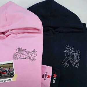 Puede incluir: Dos sudaderas con capucha, una rosa y otra negra, con diferentes dise&ntilde;os gr&aacute;ficos. La sudadera rosa presenta un dibujo lineal de una motocicleta, mientras que la sudadera negra presenta un dibujo lineal de dos personas conduciendo una motocicleta. La sudadera rosa tiene el texto "NW Racing" y "DKL" en la esquina inferior derecha.