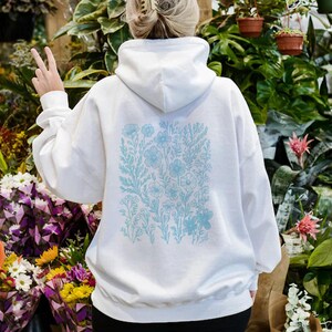 May include: White hooded sweatshirt with a blue floral print on the back. The print features a variety of flowers and leaves.