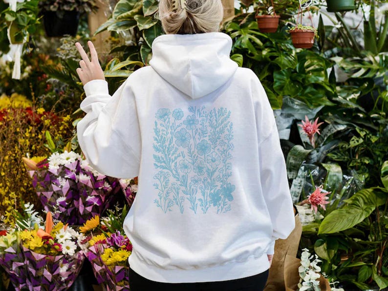 May include: White hooded sweatshirt with a blue floral print on the back. The print features a variety of flowers and leaves.
