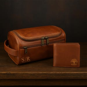 Può includere: Un set marrone in pelle composto da un beauty case e un portafoglio. Il beauty case ha una forma curva con chiusura a zip e manico. Il portafoglio è rettangolare con un disegno ad albero e il nome "DAISY". La borsa è personalizzata con le iniziali "S|R" e i nomi "susan & richard".