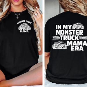 Może przedstawiać: Czarny t-shirt z białym nadrukiem monster trucka i napisem "MONSTER TRUCK MAMA" z przodu. Tył koszulki zawiera napis "IN MY MONSTER TRUCK MAMA ERA" z ilustracjami monster trucków.