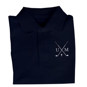 K&ouml;nnte beinhalten: Ein marineblaues Poloshirt mit einem wei&szlig;en gestickten Logo, das gekreuzte Golfschl&auml;ger und die Buchstaben "UM" zeigt.