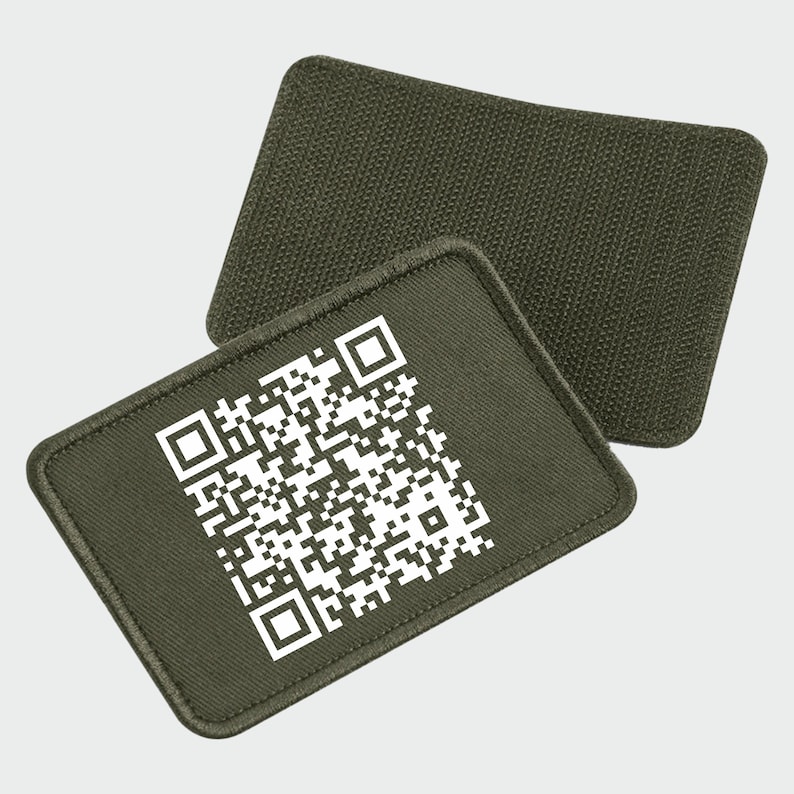 May include: A green fabric patch with a white QR code printed on it. The patch has a rough texture and is designed to be sewn onto clothing or gear.