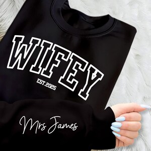 May include: Black sweatshirt with white text that reads "WIFEY EST. 2025" and "Mrs. James" on the sleeve.
