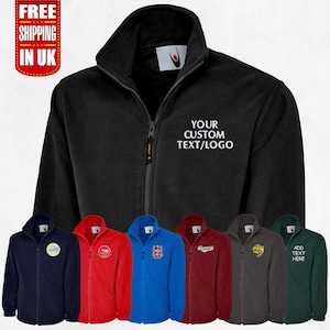 May include: A black fleece jacket with a zipper closure and a white embroidered text that says "YOUR CUSTOM TEXT/LOGO". The jacket is shown in multiple colors, including navy blue, red, blue, maroon, gray, and green.