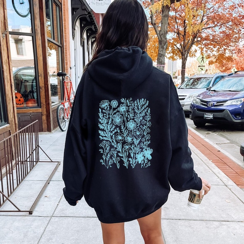 May include: Black oversized hoodie with a blue floral design on the back. The hoodie has a drawstring hood and a kangaroo pocket.