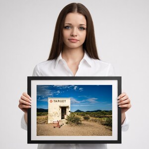 A woman holding a framed photograph of a Target building in a desert landscape.