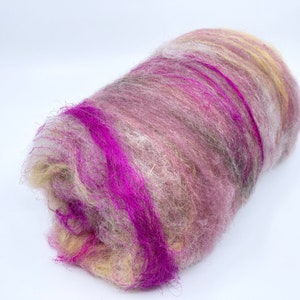 Könnte beinhalten: Eine Rolle bunte Wollvlies in den Farben Rosa, Lila, Weiß und Beige. Das Vlies ist weich und flauschig, perfekt zum Spinnen oder Filzen.