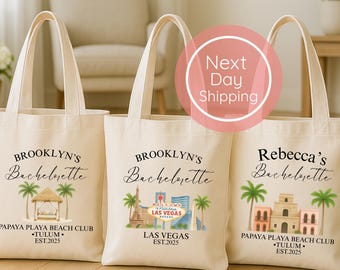May include: Three off-white canvas tote bags featuring black text and colorful illustrations. The bags display custom bachelorette party designs with locations like Tulum and Las Vegas, palm trees, and architectural landmarks.