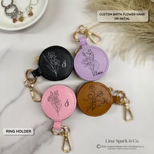 May include: Four round, zippered ring holder cases in black, lavender, light pink, and brown leather-like material. Each features a gold-tone metal clasp and a custom line-art floral design with a letter or name. Text includes CUSTOM BIRTH FLOWER NAME OR INITIAL and RING HOLDER.