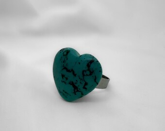 Può includere: Un anello a forma di cuore color turchese con una fascia argentata.
