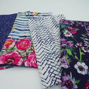 May include: A collection of folded fabric samples showcasing various patterns. Designs include a blue dotted pattern, floral prints with pink roses, a white and blue zigzag pattern, and a dark floral print with purple and red flowers.