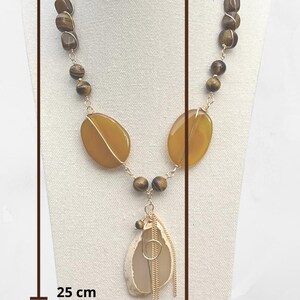 K&ouml;nnte beinhalten: Eine handgefertigte Halskette mit einer Kombination aus braunen und gelben Edelsteinen. Die Halskette umfasst ovale gelbe Steine, braune Perlen und einen Anh&auml;nger mit goldfarbenen Akzenten. Die Halskette ist etwa 25 cm bis 28 cm lang.