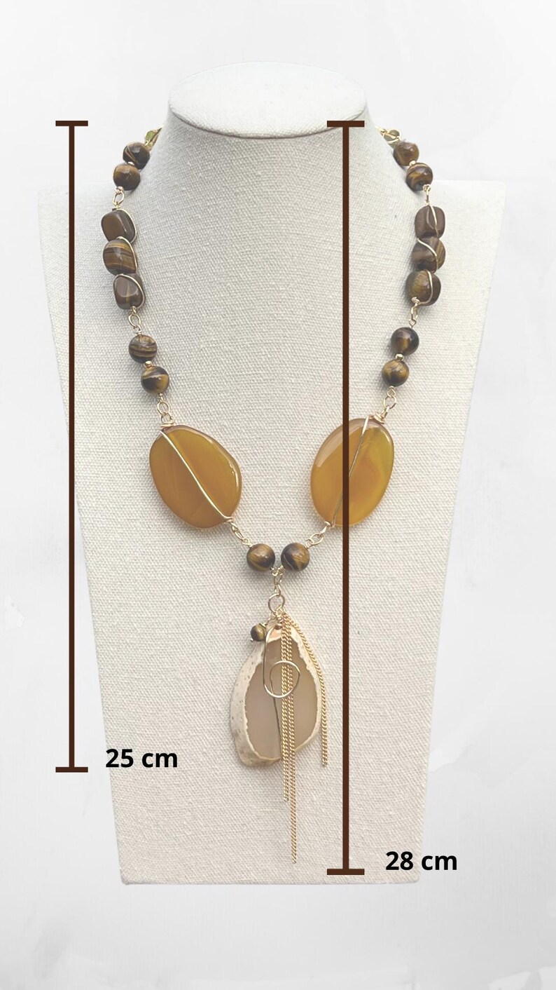 K&ouml;nnte beinhalten: Eine handgefertigte Halskette mit einer Kombination aus braunen und gelben Edelsteinen. Die Halskette umfasst ovale gelbe Steine, braune Perlen und einen Anh&auml;nger mit goldfarbenen Akzenten. Die Halskette ist etwa 25 cm bis 28 cm lang.