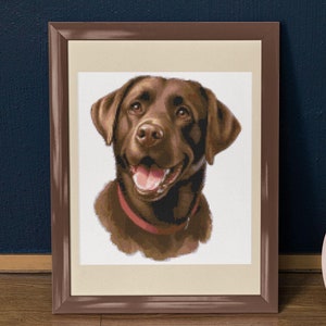 May include: A framed cross-stitch portrait of a brown Labrador Retriever with a red collar. The dog is looking up and smiling.