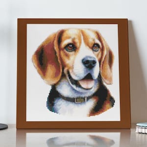 May include: A framed cross-stitch portrait of a Beagle dog. The dog has brown and white fur, with a black collar. The portrait is in a brown frame and is displayed on a light-coloured surface.
