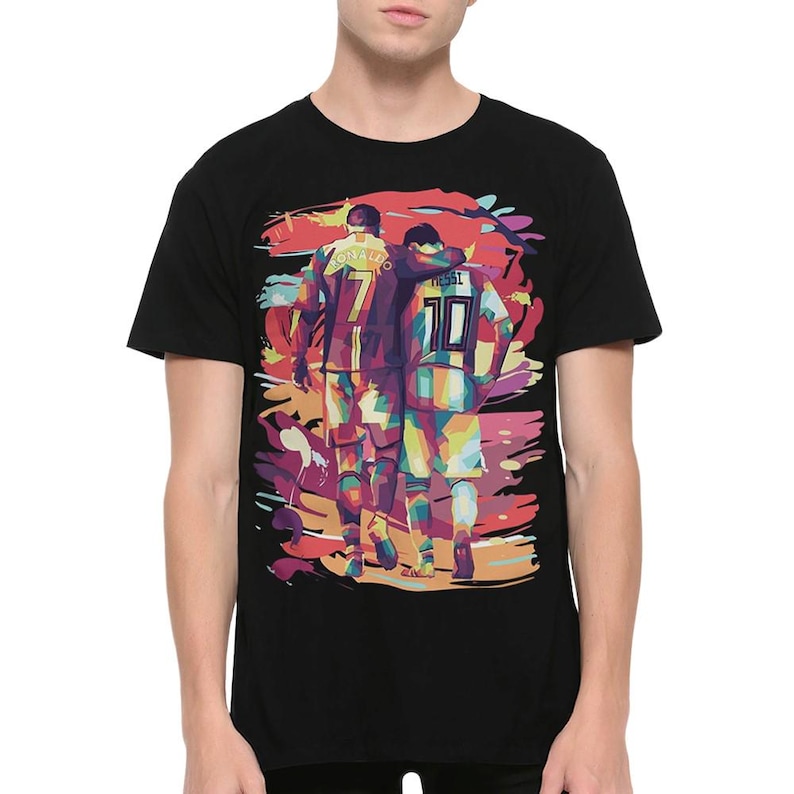 May include: Black t-shirt with a colorful graphic print of two soccer players, Cristiano Ronaldo and Lionel Messi, walking side-by-side. The graphic is in a pop art style with bold colors and outlines.