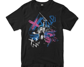 May include: Black t-shirt featuring a graphic print of a woman with blue hair holding a weapon. The graphic is in pink, blue, and white with the word "Riot" written in blue.