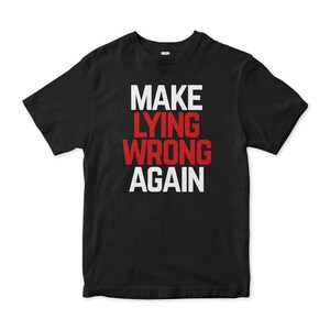 Może przedstawiać: Czarny t-shirt z napisem "MAKE LYING WRONG AGAIN" wydrukowanym białymi i czerwonymi literami. Koszulka ma okrągły dekolt i wydaje się być wykonana z bawełny.
