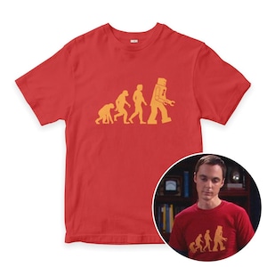 May include: Red t-shirt featuring a yellow graphic of the evolution of man, culminating in a robot. The design is centered on the front of the shirt. The shirt is made of a soft material.