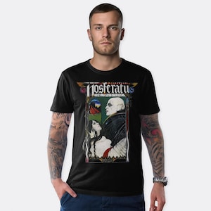 May include: Black t-shirt featuring a graphic print of a vampire and a woman. The graphic is in a colourful art deco style and includes the text "Nosferatu The Vampire".