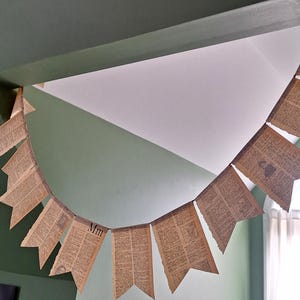 May include: A banner of pennant-shaped flags made from aged book pages. The flags are strung together, with the letter "Mm" visible on one. The banner hangs against a green and white wall.