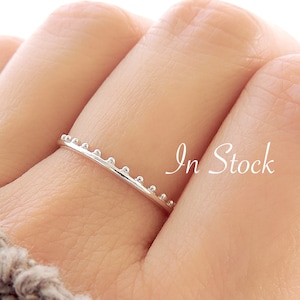 May include: A thin silver ring with a row of small beads around the band. The ring is on a finger.