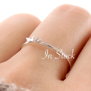 May include: A delicate silver ring with a butterfly design. The ring is thin and simple, with a small butterfly charm on the band.