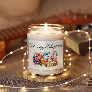 May include: A white candle with a label that says "He is my Shepherd". The label features a watercolor illustration of a lamb, a cross, a bible, and flowers.