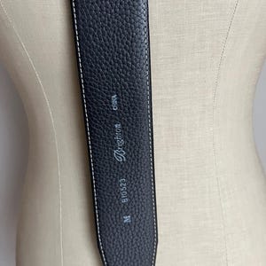 Puede incluir: Cintur&oacute;n de cuero negro con costuras blancas. El cintur&oacute;n tiene una superficie texturizada y la marca "Brighton" es visible. El cintur&oacute;n est&aacute; marcado con "M", "B10523" y "CHINA".