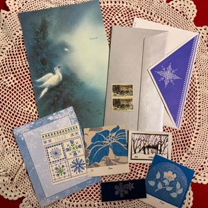 May include: A collection of vintage Christmas cards and stationery. The cards feature illustrations of doves, snowflakes, and floral designs in shades of blue and white. Includes envelopes and stamps.