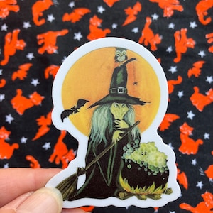 May include: A witch with a green dress and a pointed hat stirs a cauldron with a bubbling green potion. An owl sits on the top of the witch's hat. The scene is set against a full moon.