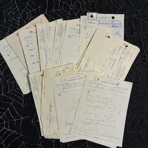 May include: A collection of vintage off-white paper prescription pads from Johnson's Pharmacy, featuring blue printed text, headers, and handwritten medical instructions in blue and black ink. Each rectangular slip has a hole punched at the top.