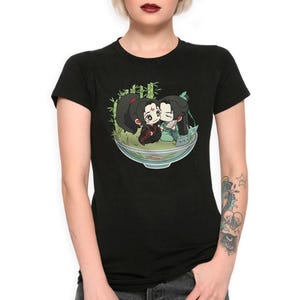 Puede incluir: Camiseta negra con un estampado gráfico de dos personajes de anime en un cuenco con follaje verde. Los personajes se besan y tienen el pelo negro. El cuenco es blanco con un borde verde.