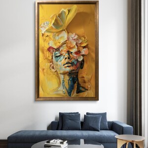 Op de afbeelding: Een schilderij van een vrouwenhoofd met bloemen op haar hoofd. De achtergrond is geel en het gezicht van de vrouw is geschilderd in tinten blauw, groen en geel.