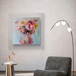 Puede incluir: Una pintura enmarcada de dos mujeres con flores en la cabeza. Las mujeres miran hacia adelante y las flores son rosas, blancas y amarillas. El fondo es de color azul claro.