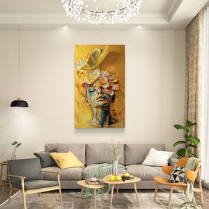 Op de afbeelding: Een schilderij van een vrouwen gezicht met bloemen die haar ogen bedekken. De achtergrond is heldergeel.