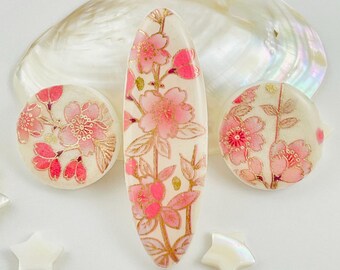 以下が含まれることがあります： クリーム色のベースにピンクの桜模様と金色の輪郭が描かれたヘアアクセサリー3点セット。細長い楕円形のヘアクリップ1点と、円形のヘアクリップ2点で構成されており、すべてに花柄が施されています。