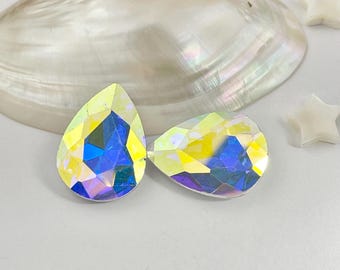 以下が含まれることがあります： 青、黄、紫の色合いを反射する虹色の仕上げが施された、洋ナシ型のファセットカットクリスタル2個。クリスタルは平らな裏面と尖った上部を持ち、幾何学的なファセットを備えた光沢のある反射面を見せています。