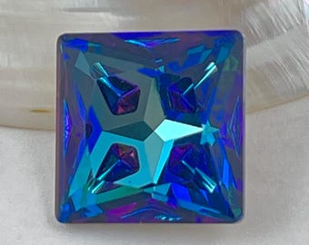 以下が含まれることがあります： 複雑なファセットデザインの、正方形にカットされた虹色の宝石。青、緑、紫など、さまざまな色が表示され、中央には星のような模様があります。宝石は、柔らかく真珠のような背景に配置されています。