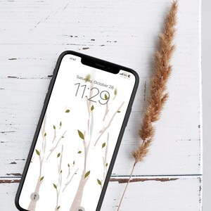 May include: A black smartphone with a white background and a floral design. The time is 11:29 and the date is Saturday, October 26. The phone is lying on a white wooden surface with a dried grass stalk.